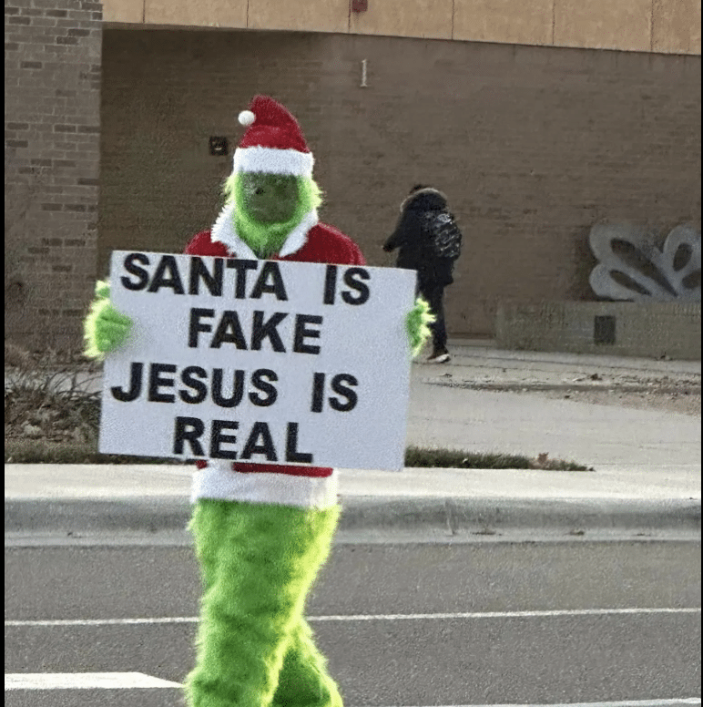 (WATCH) Texas pastor dressed as Grinch under fire after holding sign in front of elementary school saying “Santa is fake” and “Jesus is real”