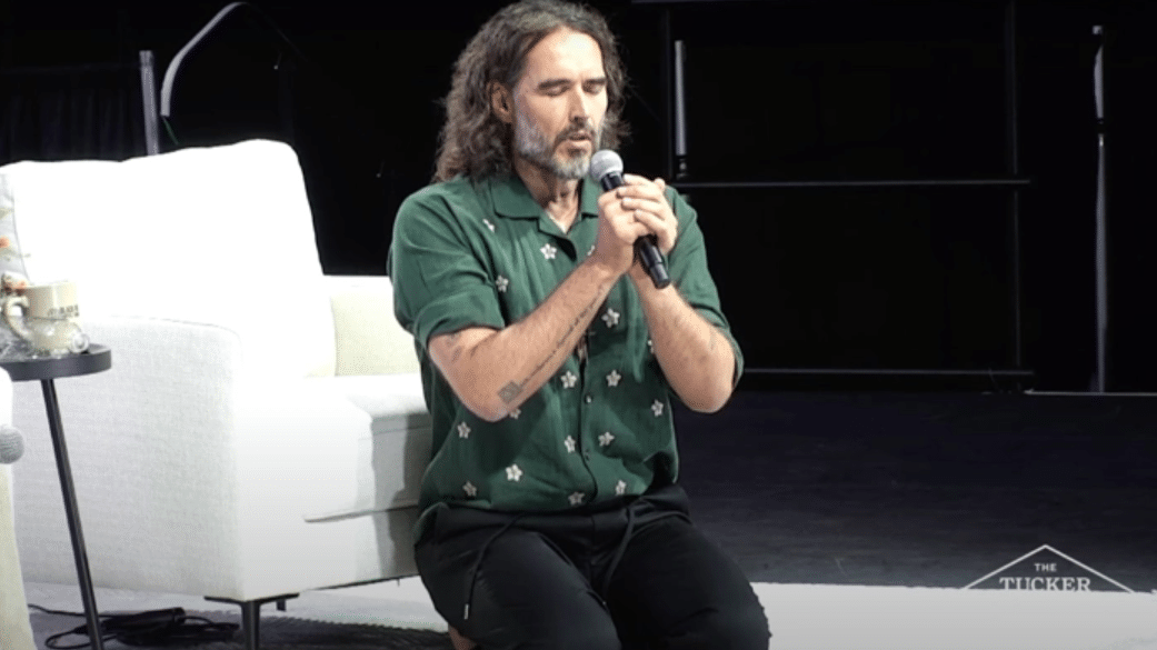 Russell Brand kneels in prayer at Tucker Carlson event, prays against ‘dark and demonic forces’